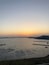 A coastal scene at sunset with a large body of water, a pier, and a distant hill.
