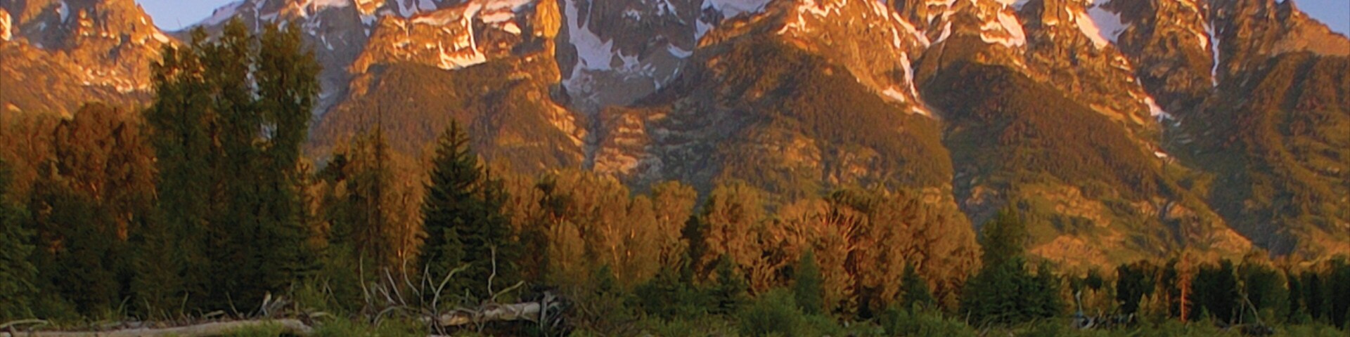Uma cordilheira com picos nevados e um lago tranquilo que reflete a paisagem.