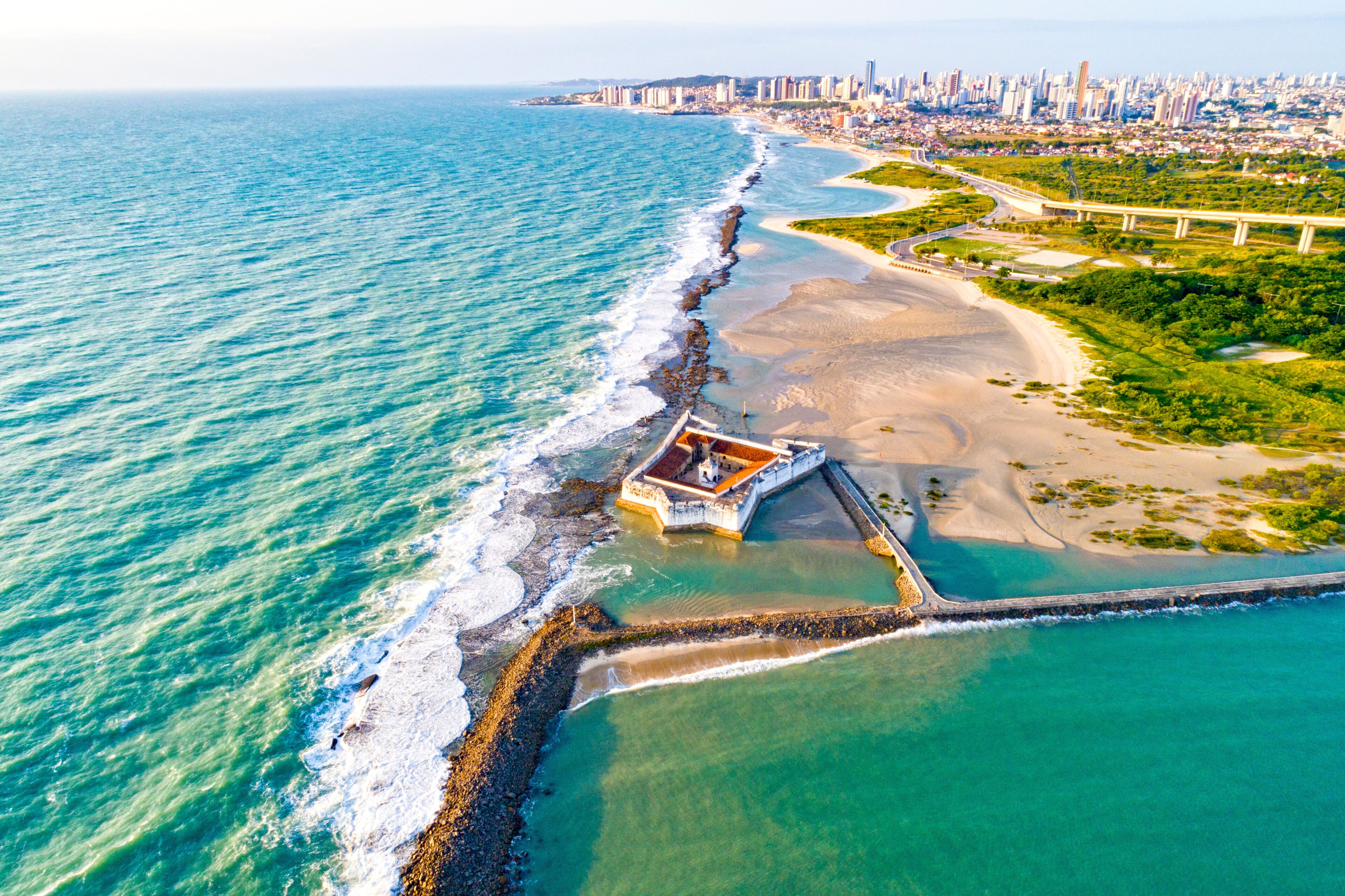 Vista aérea de una ciudad costera con playa, muelle y puente.