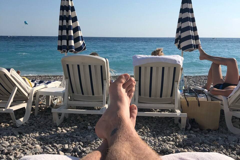 A beach with white lounge chairs and striped umbrellas.