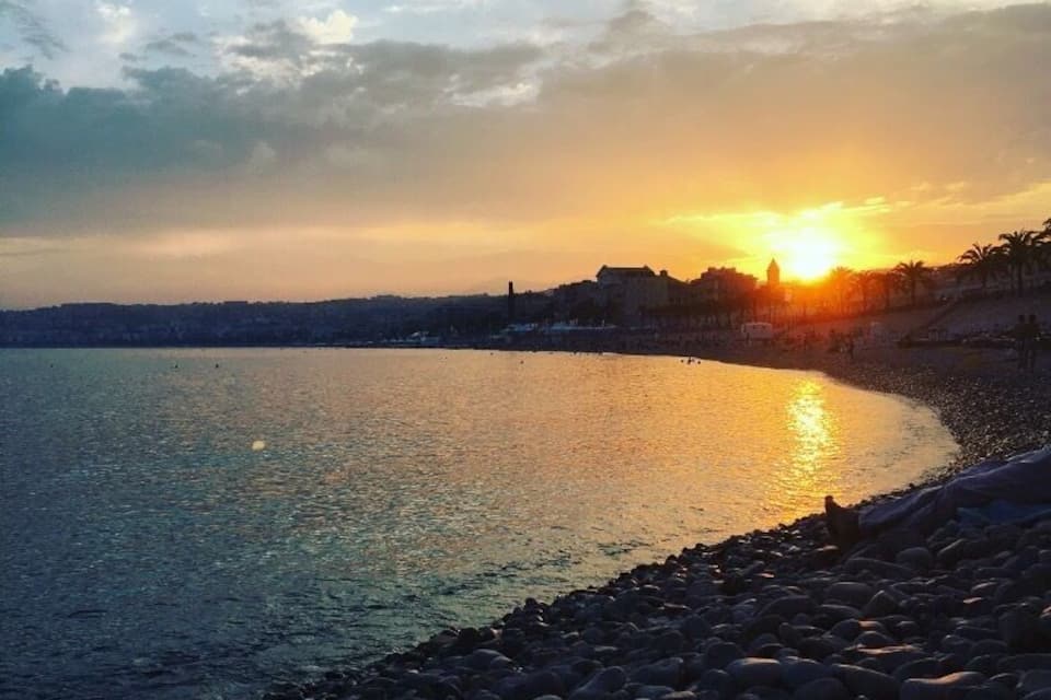 A sunset over a calm sea with a rocky shoreline and distant buildings.
