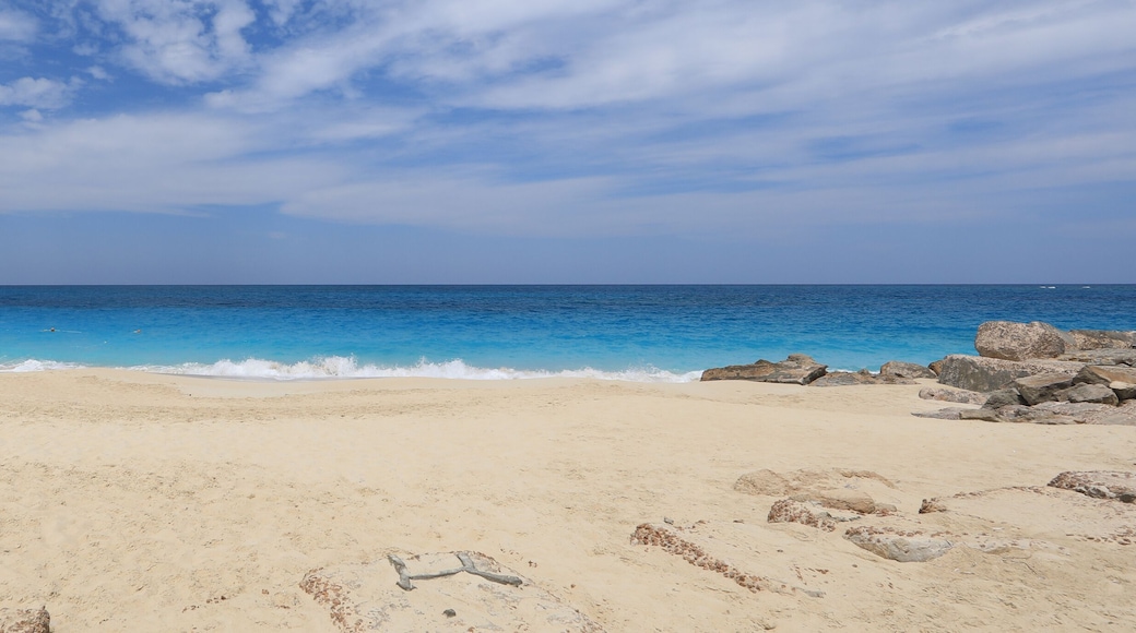 A sandy beach with clear blue water and scattered rocks.