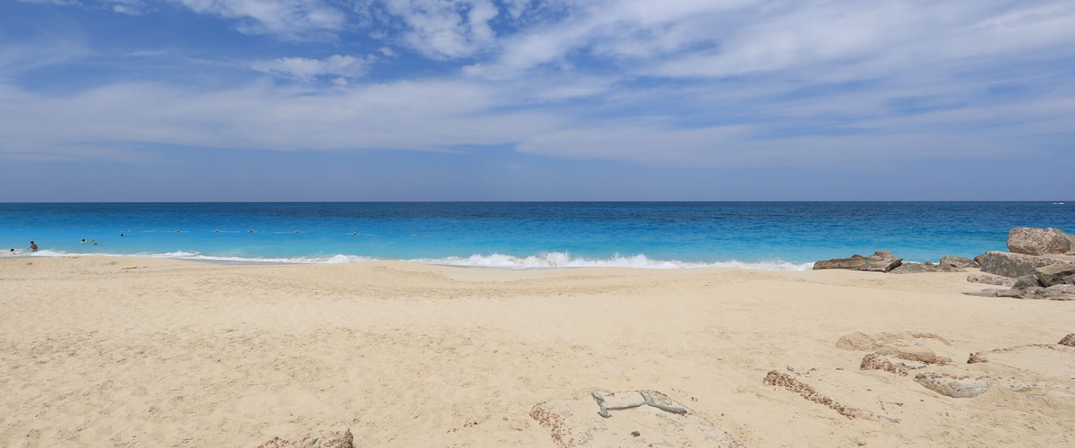 A sandy beach with clear blue water and scattered rocks.