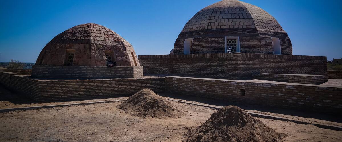 Two large stone domed structures with brick walls and a clear blue sky in the background.