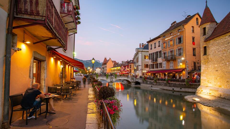 A riverside town with historic buildings, a bridge, and outdoor seating along the water.