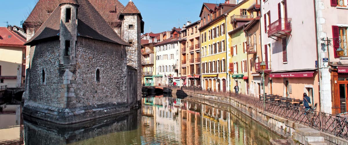 A historic stone tower with a red roof, a canal, and colorful buildings along the water's edge.