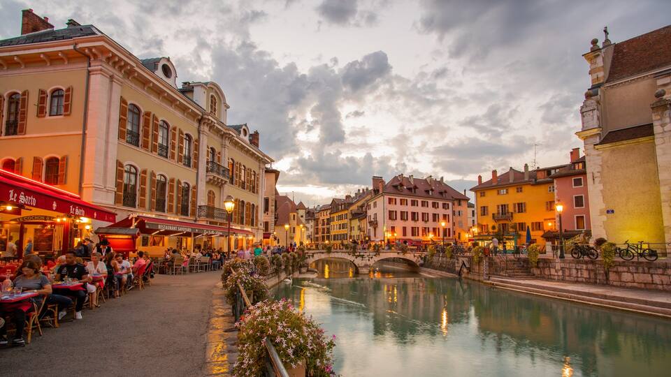 A riverside café area with outdoor seating, historic buildings, and a stone bridge.