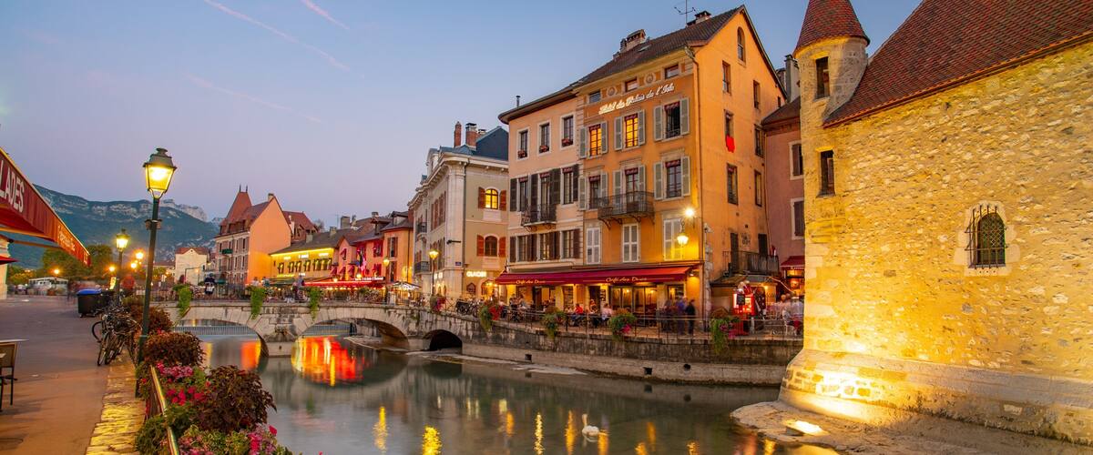 A riverside town with historic buildings, a stone bridge, and a canal reflecting the lights.