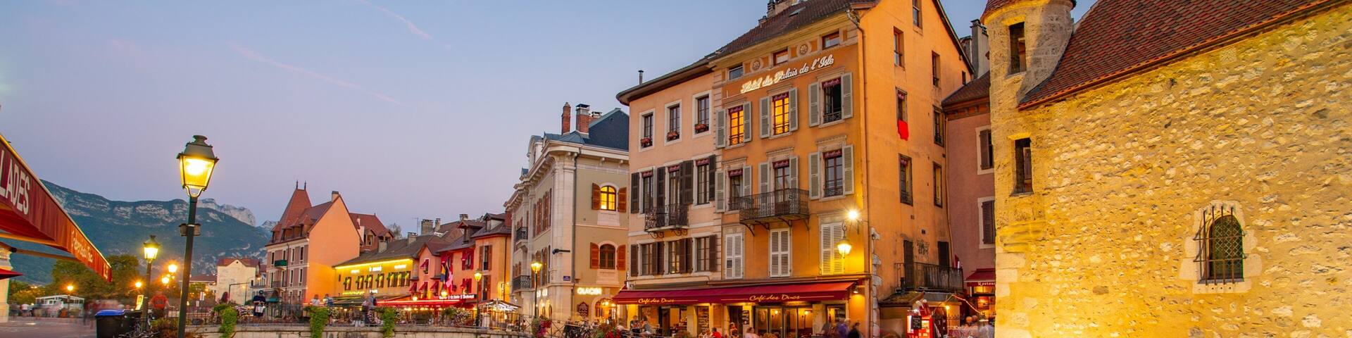 A riverside town with historic buildings, a stone bridge, and a canal reflecting the lights.