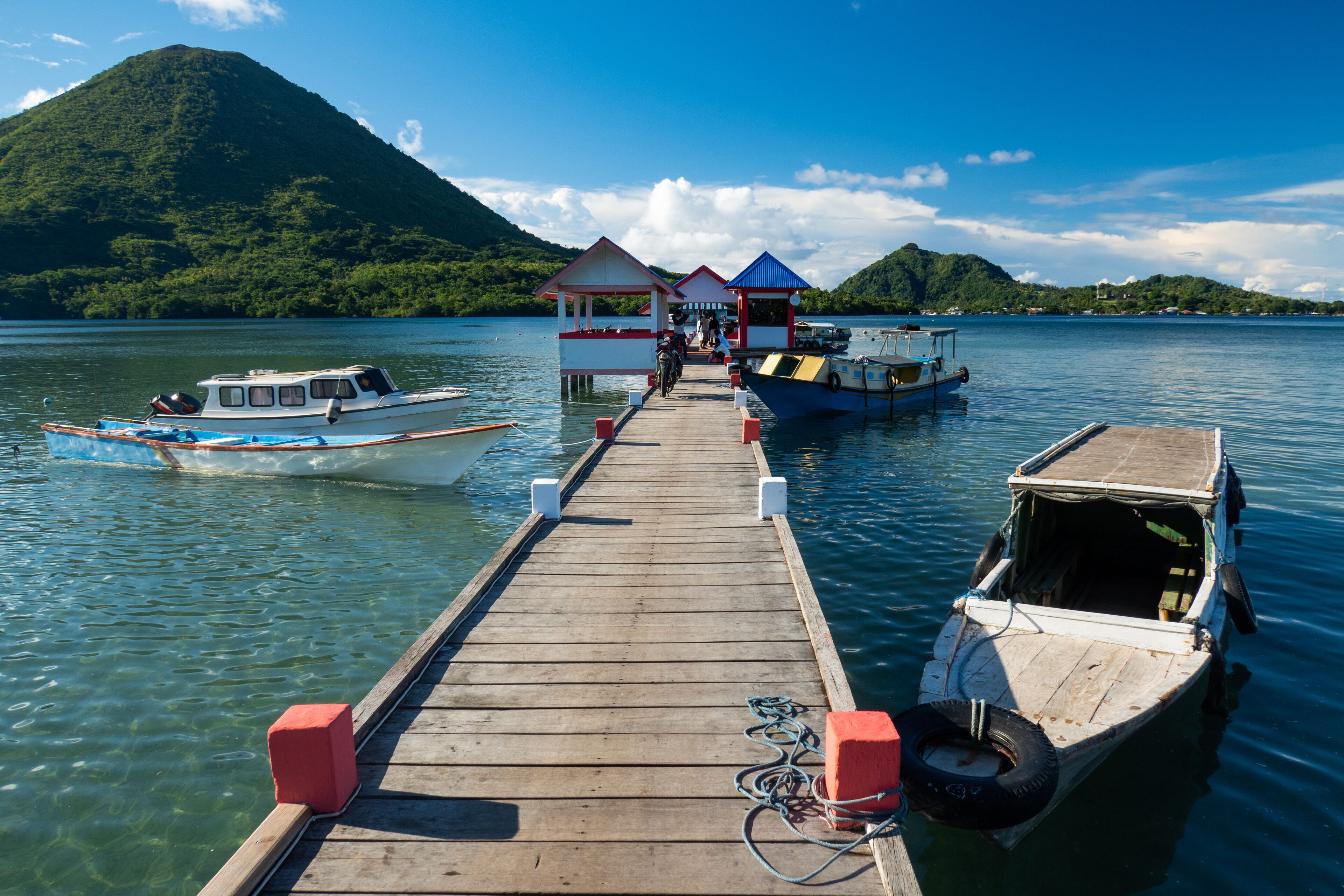 A wooden pier leading to a small island with a mountain in the background.