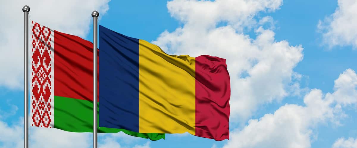 Two flags on flagpoles against a blue sky with clouds.