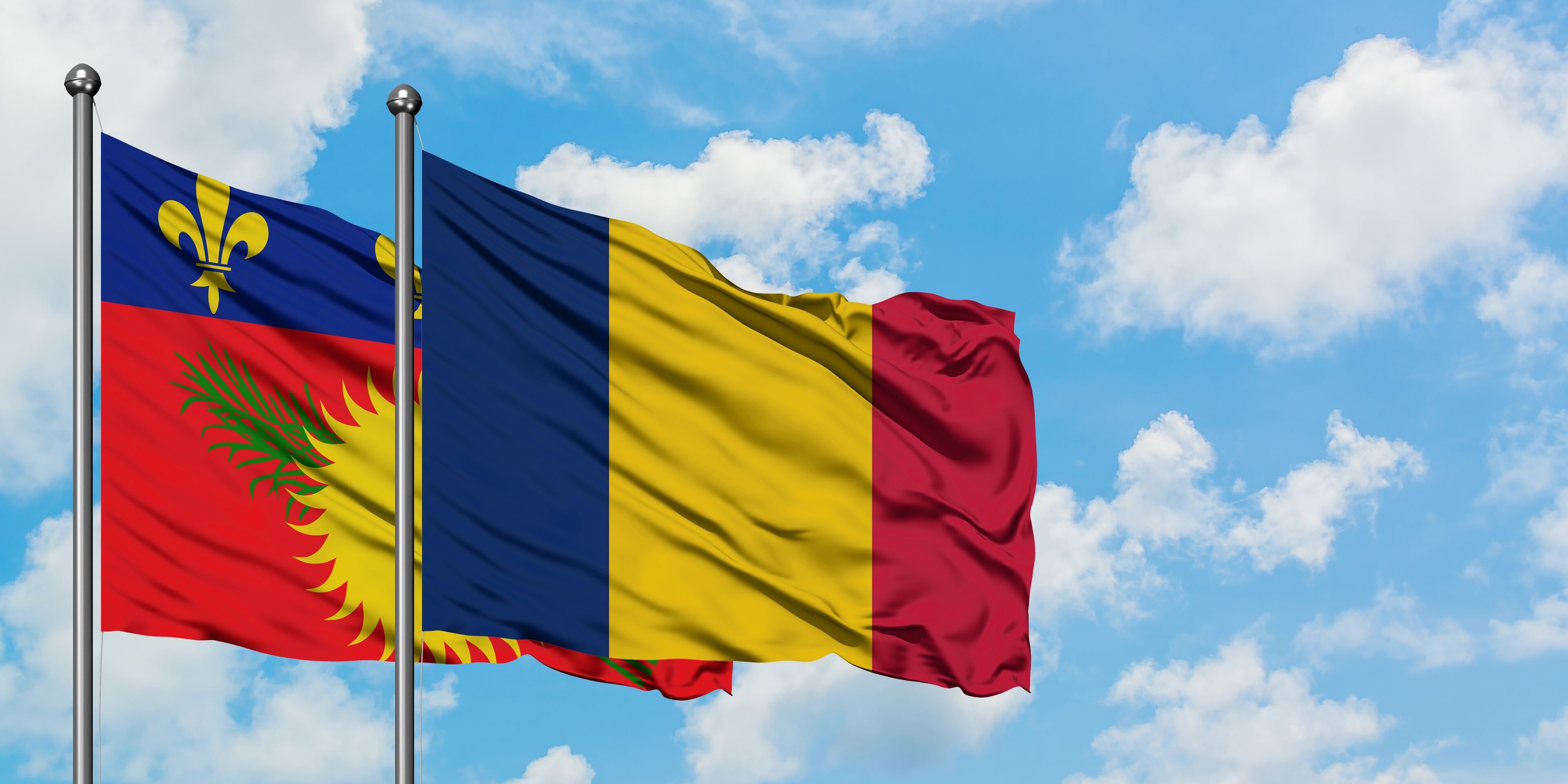 Guadeloupe and Chad flag waving in the wind against white cloudy blue sky together. Diplomacy concept, international relations.