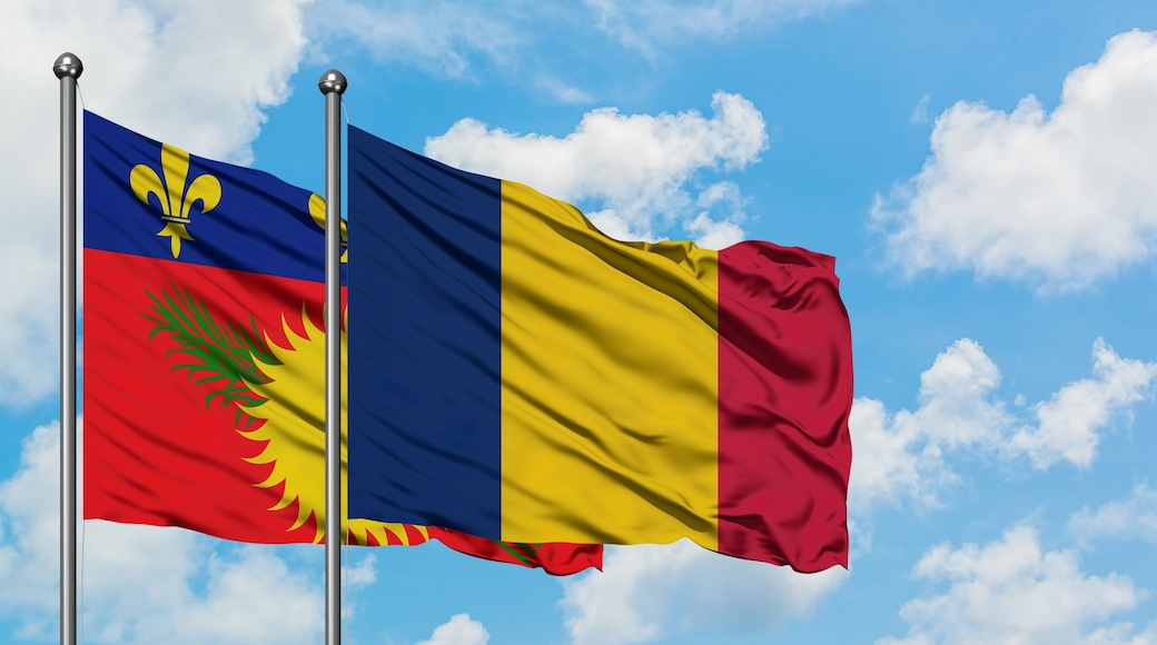 Guadeloupe and Chad flag waving in the wind against white cloudy blue sky together. Diplomacy concept, international relations.