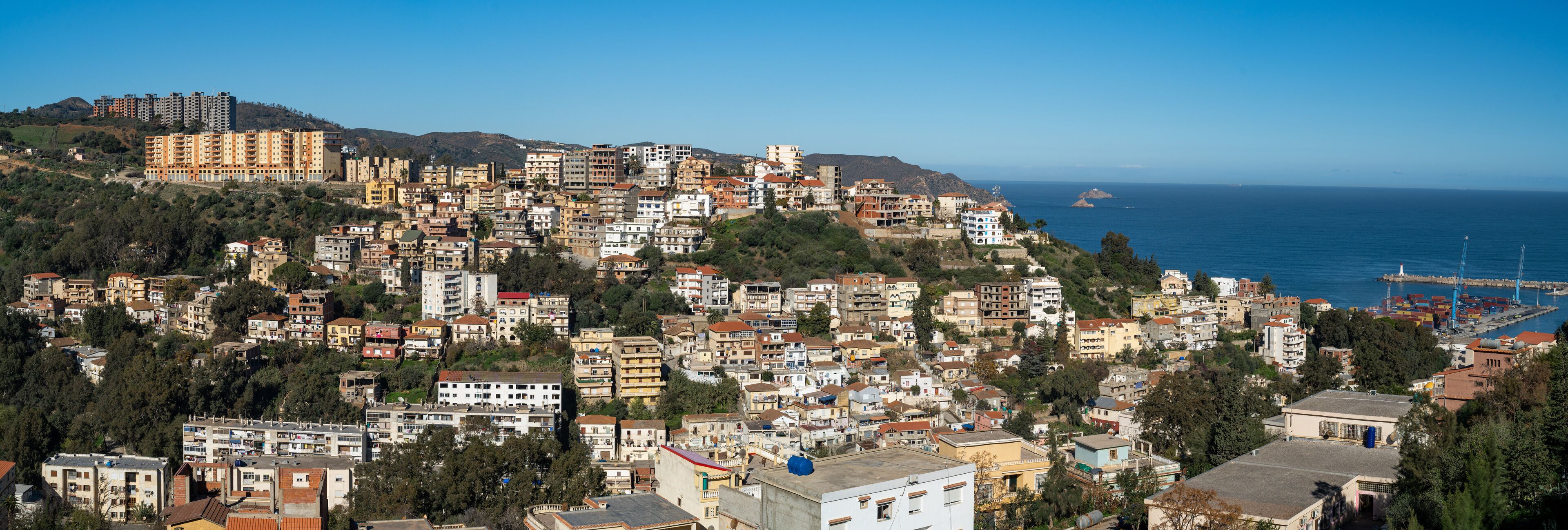 A coastal town with densely packed buildings, a clear blue sky, and the sea in the background.
