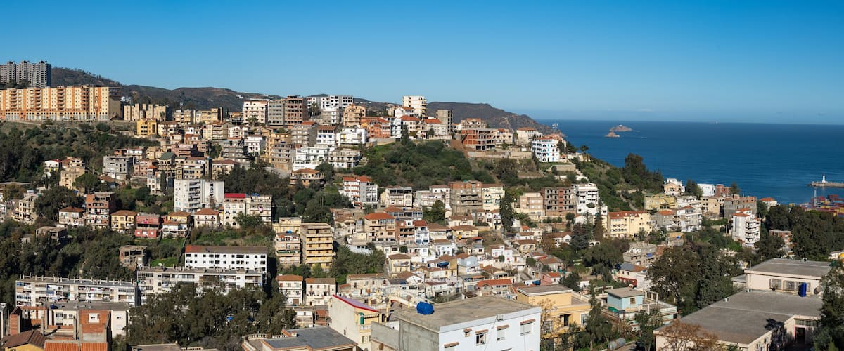 A coastal town with densely packed buildings, a clear blue sky, and the sea in the background.