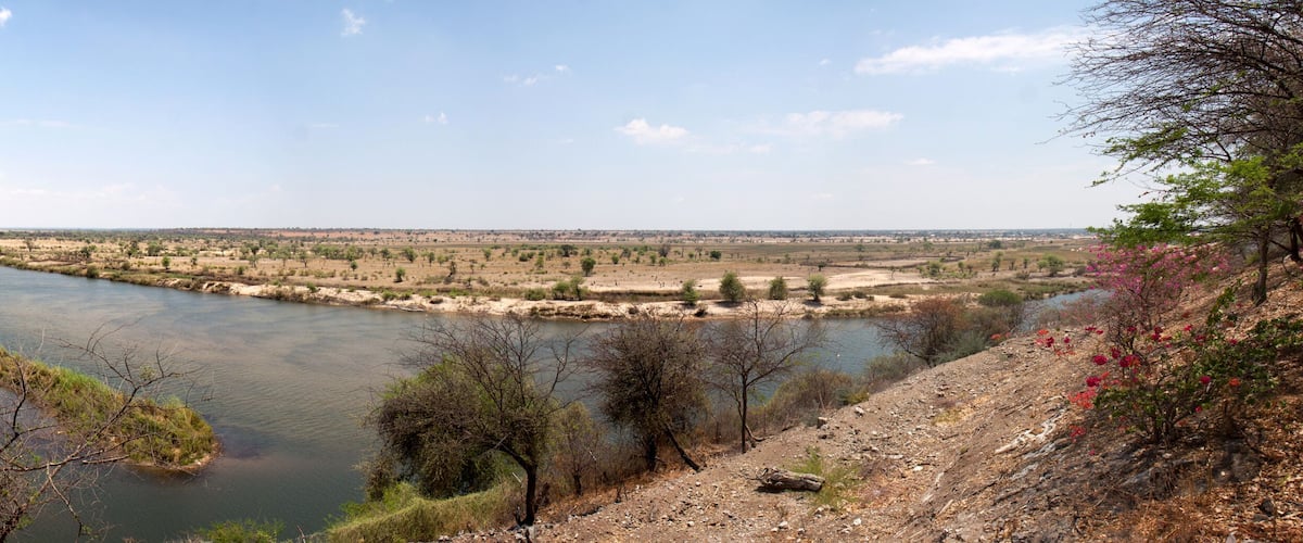 A river winding through a flat landscape with sparse vegetation and a few trees.