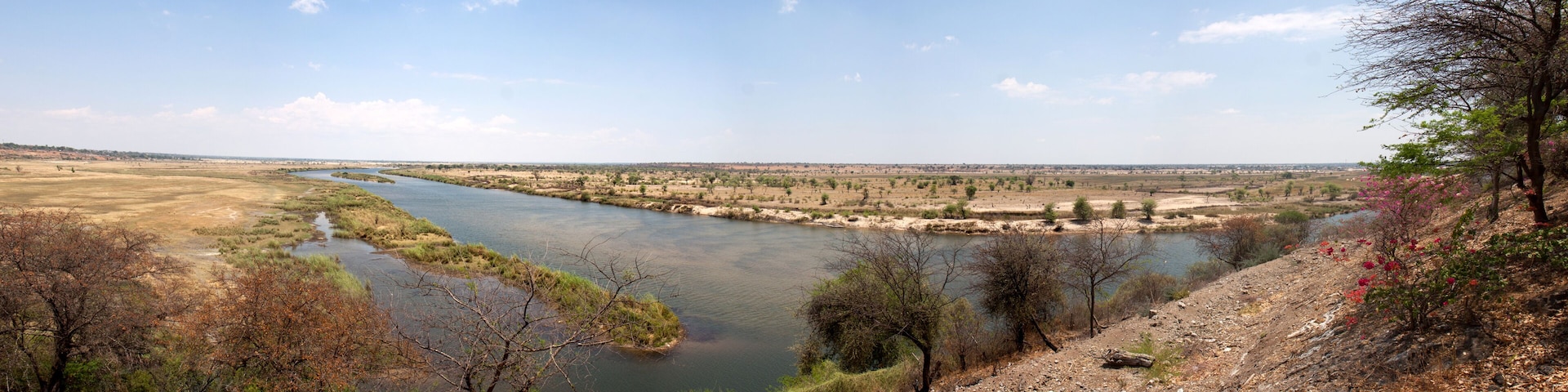 A river winding through a flat landscape with sparse vegetation and a few trees.