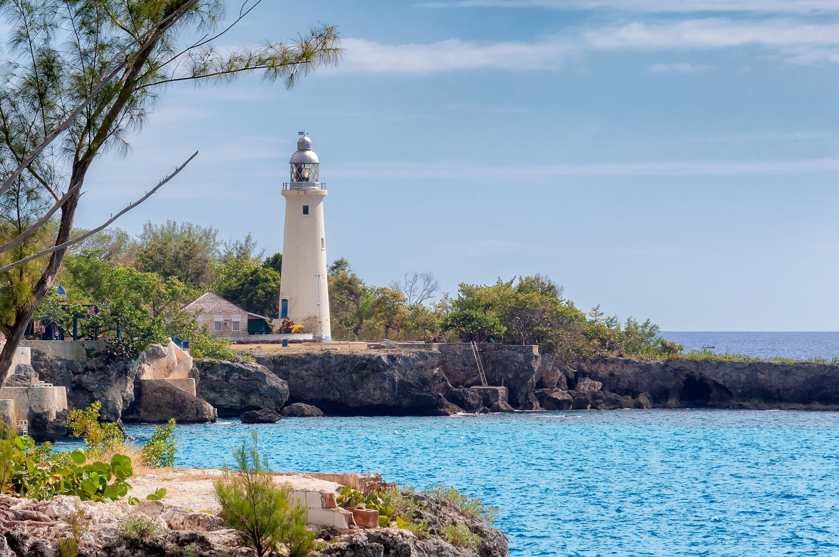 A lighthouse on a rocky coastline with clear blue waters and surrounding greenery.
