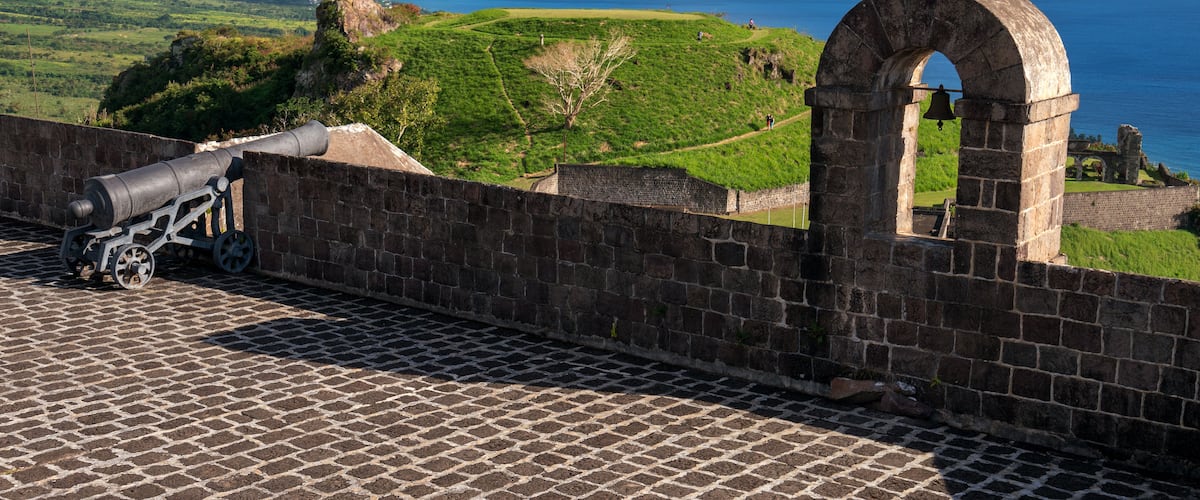 Un cannone storico su un muro in mattoni con vista sul paesaggio costiero sotto un cielo sereno.