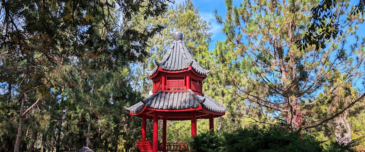 A traditional red pagoda with a tiled roof, surrounded by pine trees and rocks.
