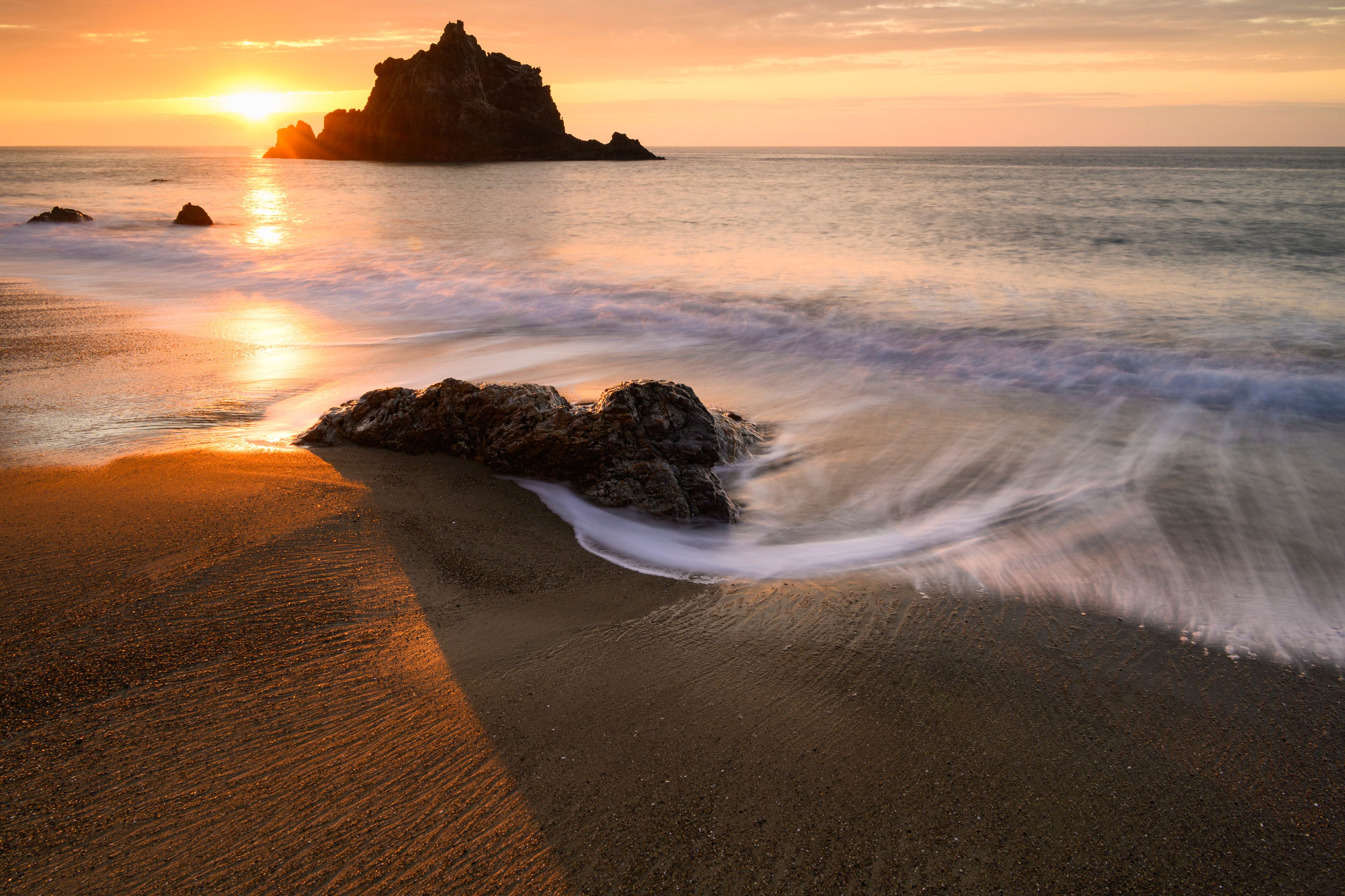 A beach with waves, rocks, and a sunset.