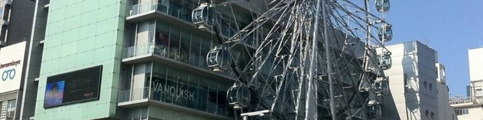 A Ferris wheel in front of a modern building with a sign that reads "VANNOUSH".