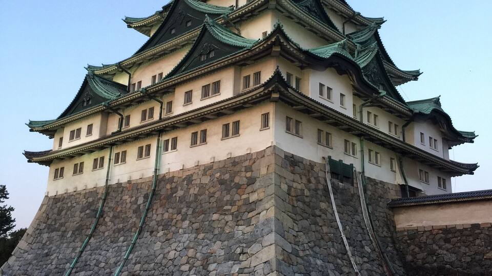A traditional Japanese castle with multiple tiers, stone base, and green-tiled roofs.