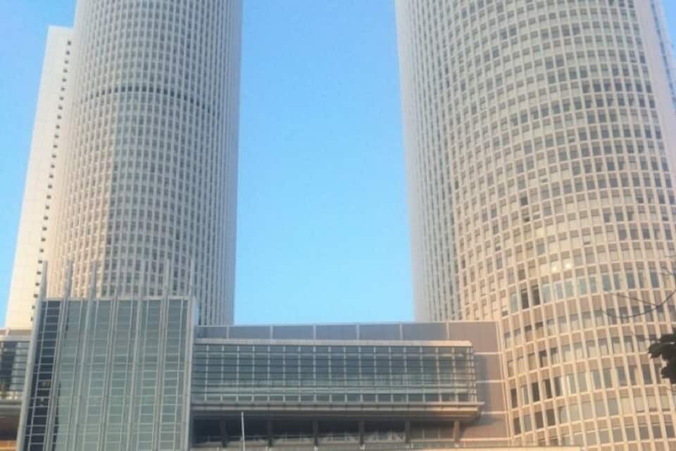 Zwei hohe, zylindrische Wolkenkratzer mit einer gitterartigen Fassade und ein modernes Gebäude mit Glasfront im Vordergrund.