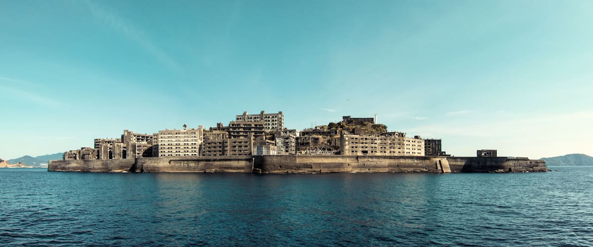A coastal fortress with multiple buildings, a large water body in the foreground, and distant islands.