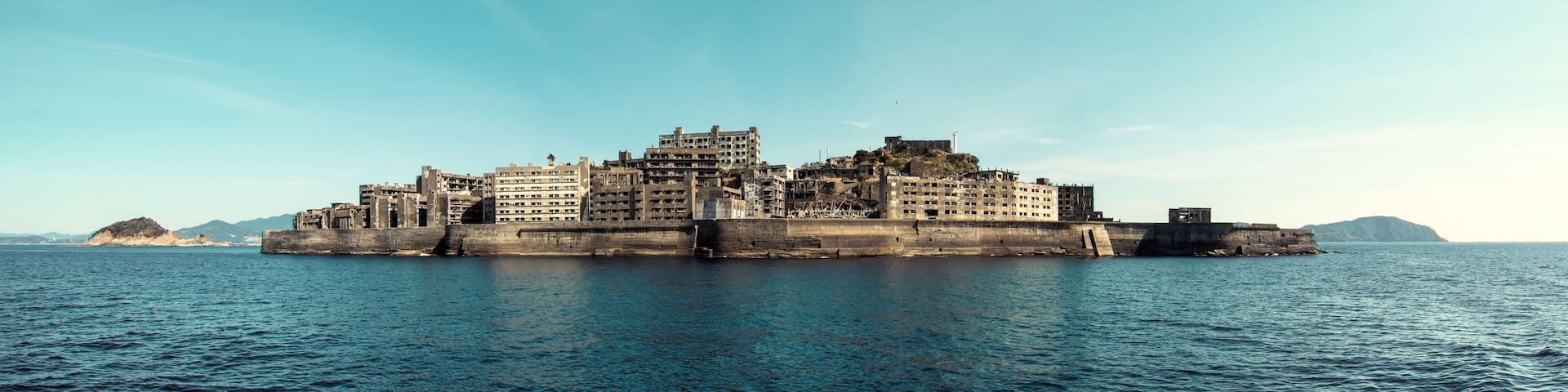 A coastal fortress with multiple buildings, a large water body in the foreground, and distant islands.