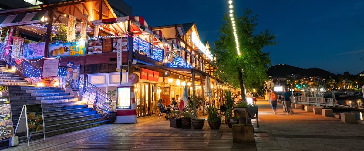 A brightly lit street with a wooden building adorned with lights and signs, a staircase, and a tree.