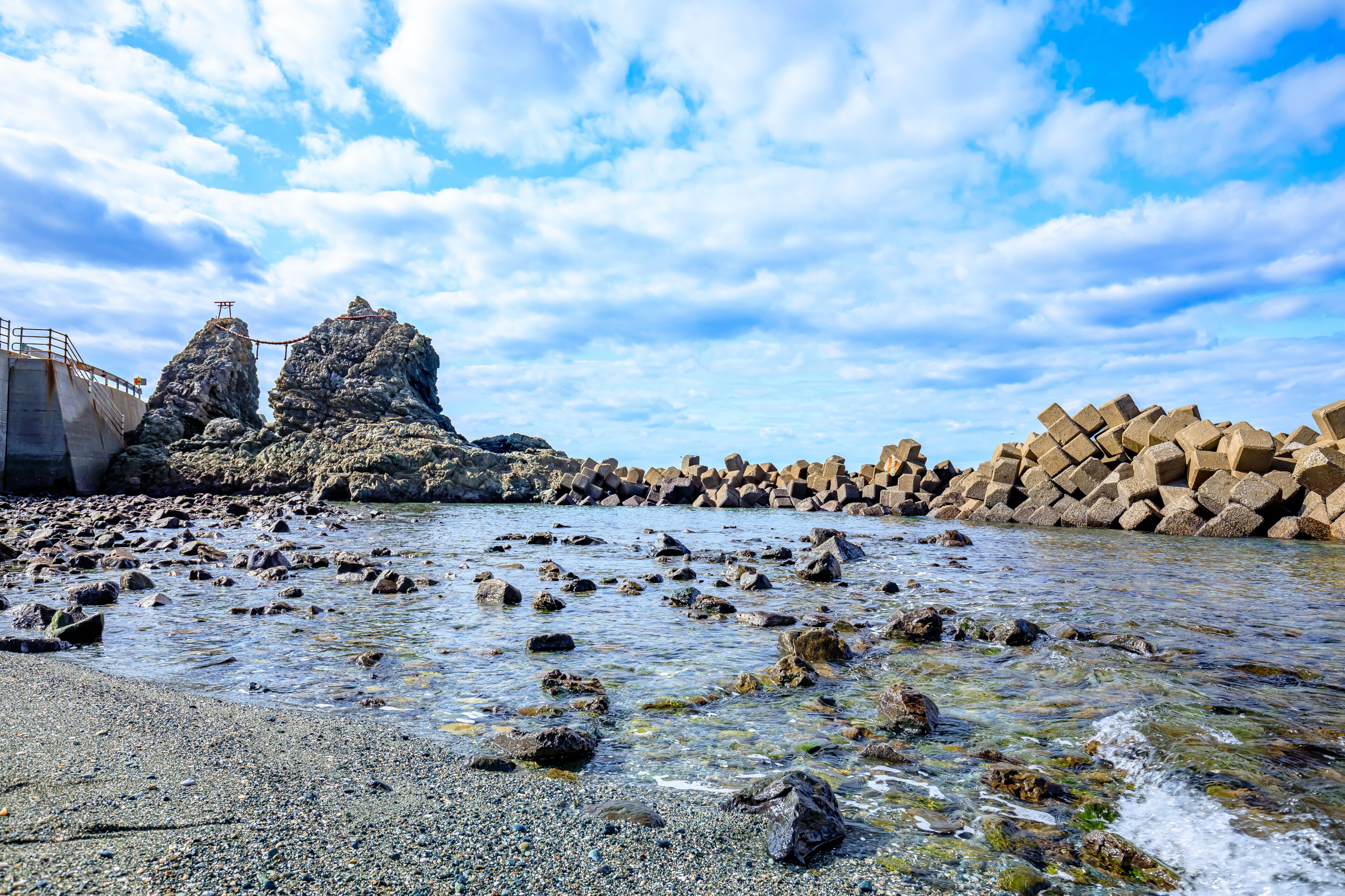 Una costa rocosa con agua cristalina, un puente y un conjunto de grandes rocas.