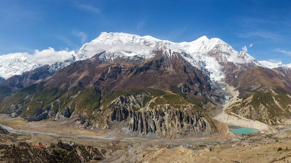 A mountainous landscape with snow-capped peaks, a valley with a turquoise lake, and a winding road.