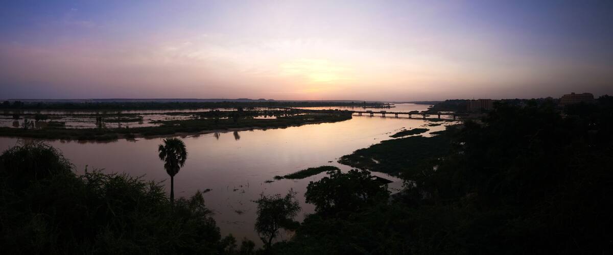 A sunset over a river with a bridge and surrounding vegetation.