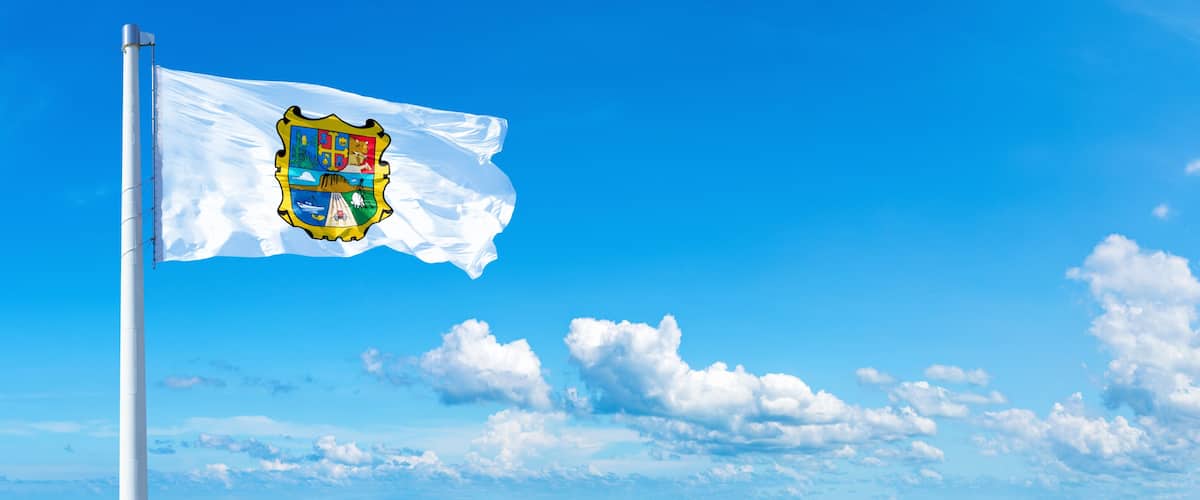 A flag on a flagpole against a clear blue sky with scattered clouds.