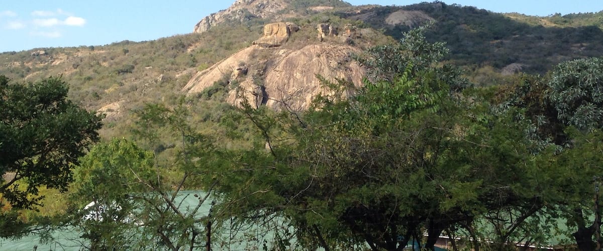 A mountain with a prominent rock formation and dense green foliage in the foreground.