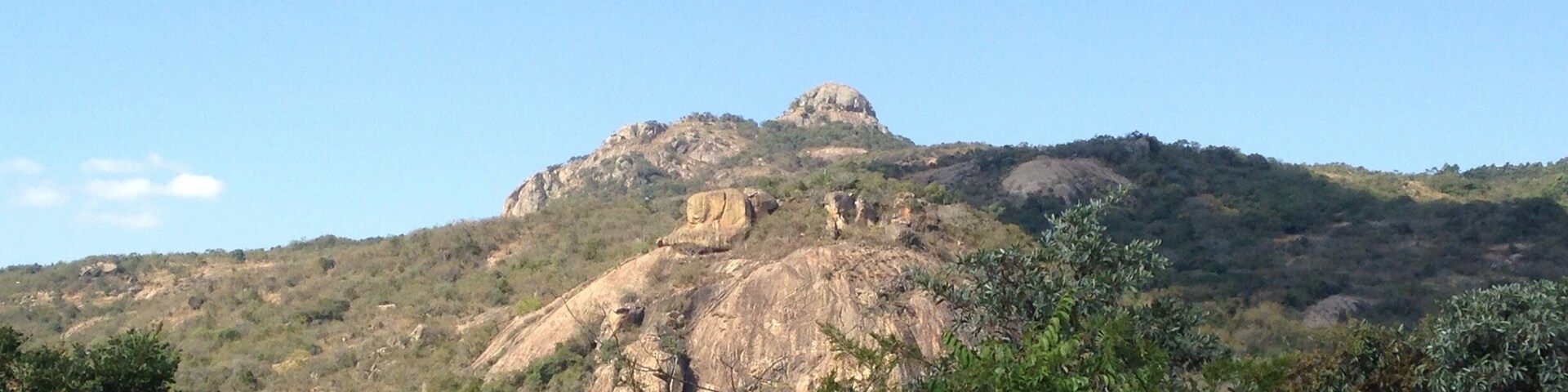 A mountain with a prominent rock formation and dense green foliage in the foreground.