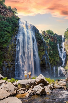 A waterfall cascading down a rocky cliff surrounded by lush greenery.