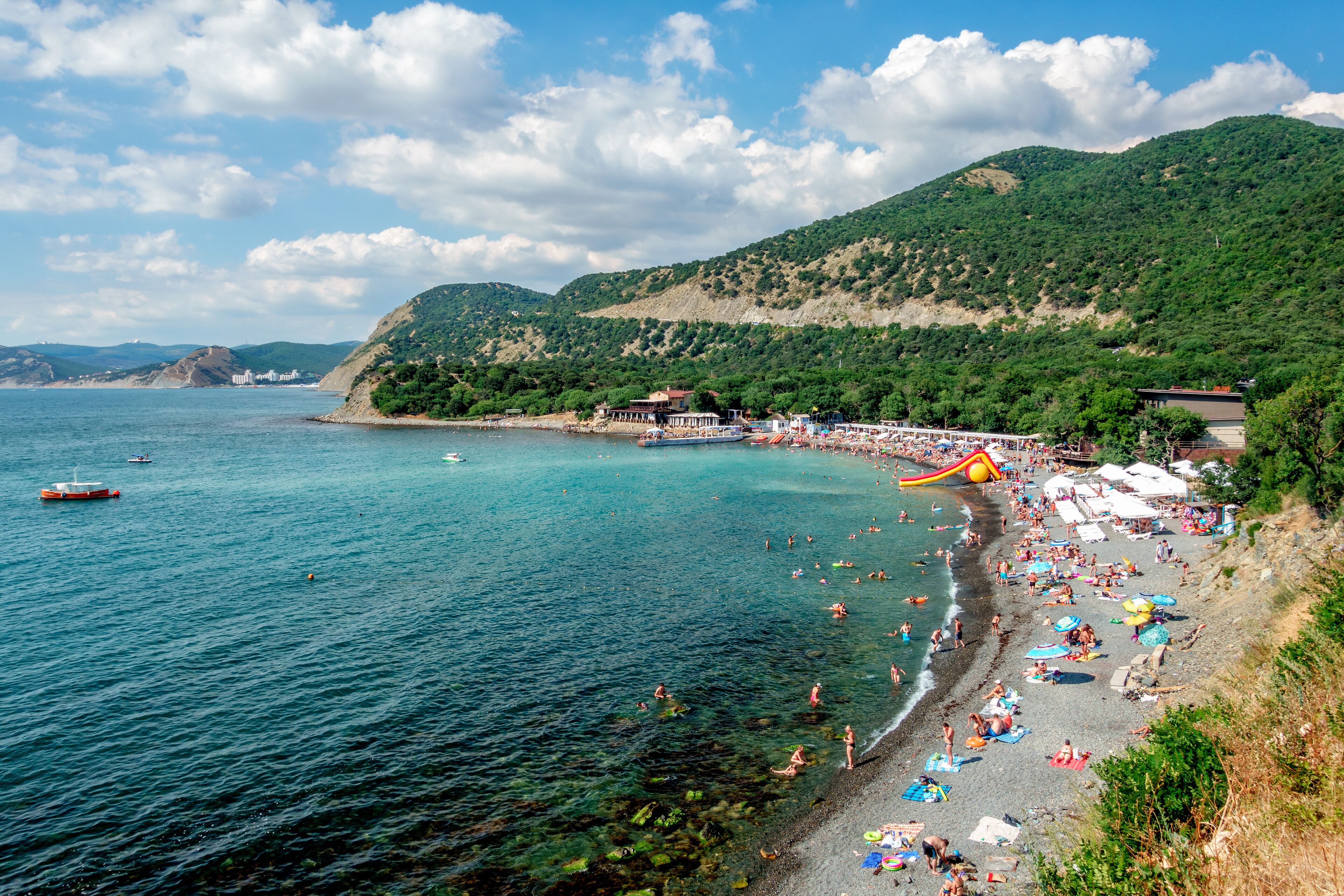 Anapa, Russia - July 12, 2019: Stony beach of Black Sea coast in Bolshoy Utrish village full of people on bright sunny summer day. Aerial view