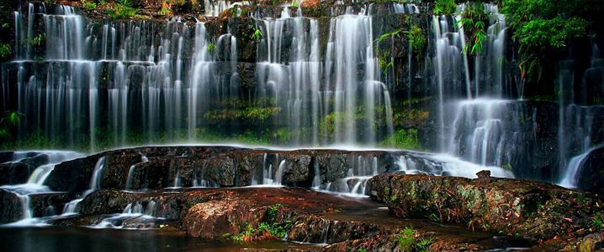 A multi-tiered waterfall with cascading water over rocks and lush greenery.