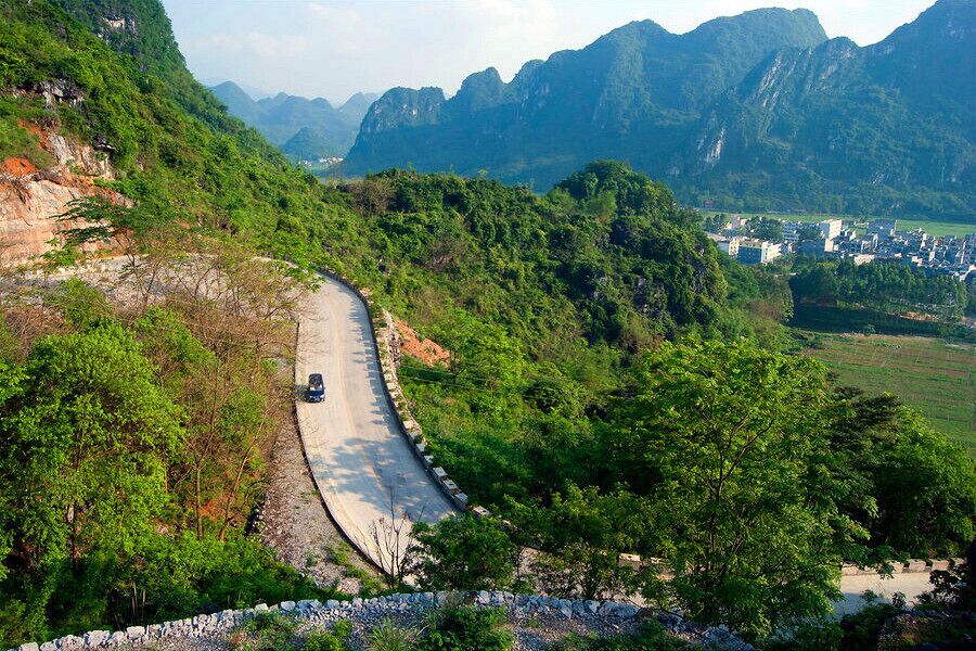 A winding road through a mountainous landscape with lush greenery and distant buildings.