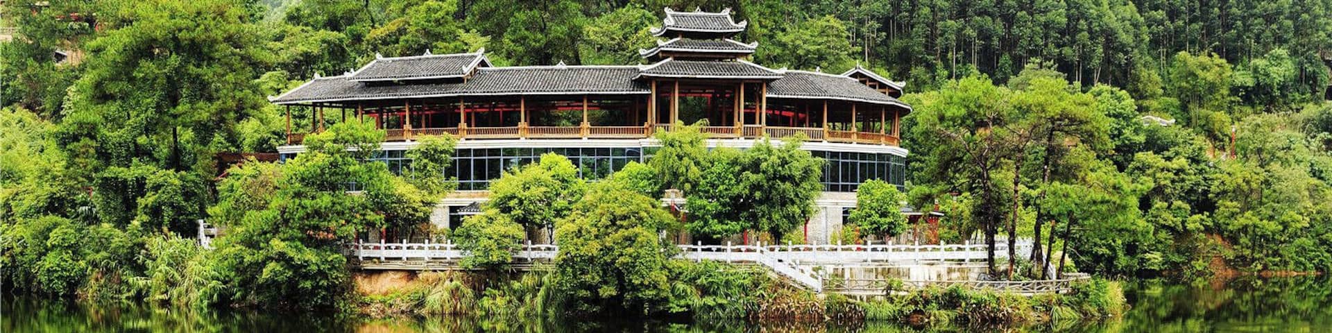 A traditional wooden building with a tiled roof, surrounded by lush greenery and a calm lake.
