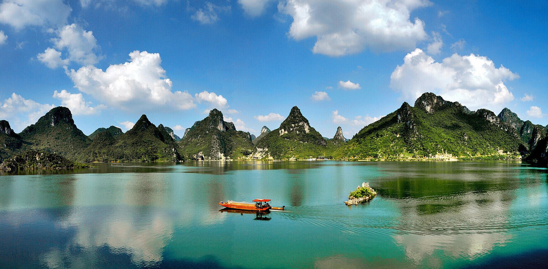 Um lago tranquilo com um barco, rodeado por montanhas verdes e céu azul límpido.