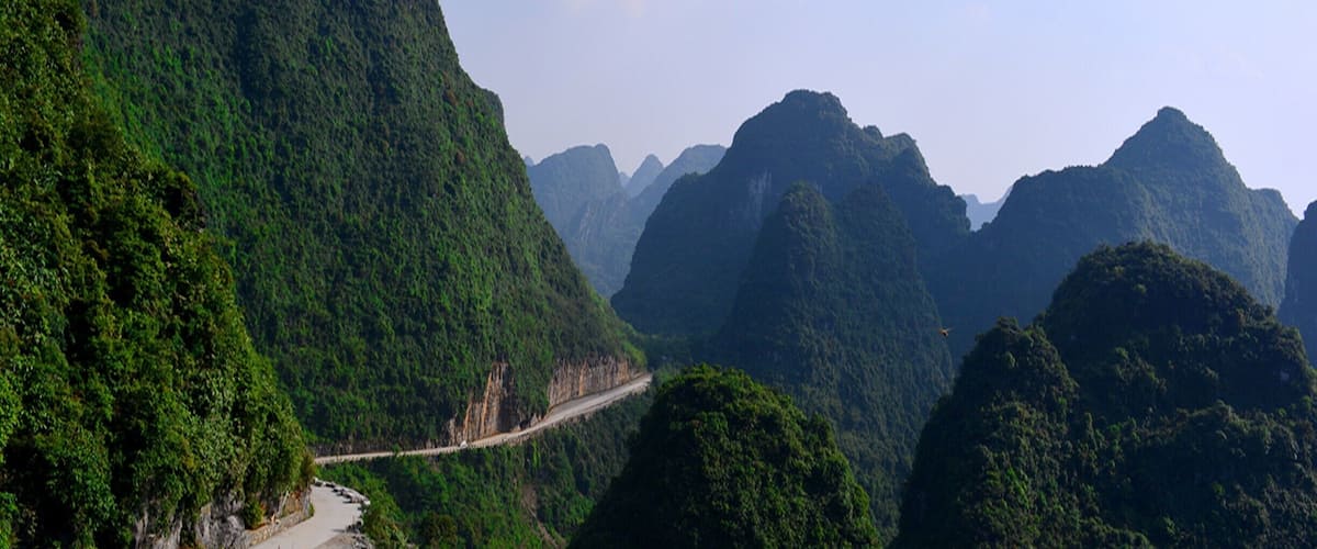 A winding road through a mountainous landscape with lush greenery and rugged terrain.