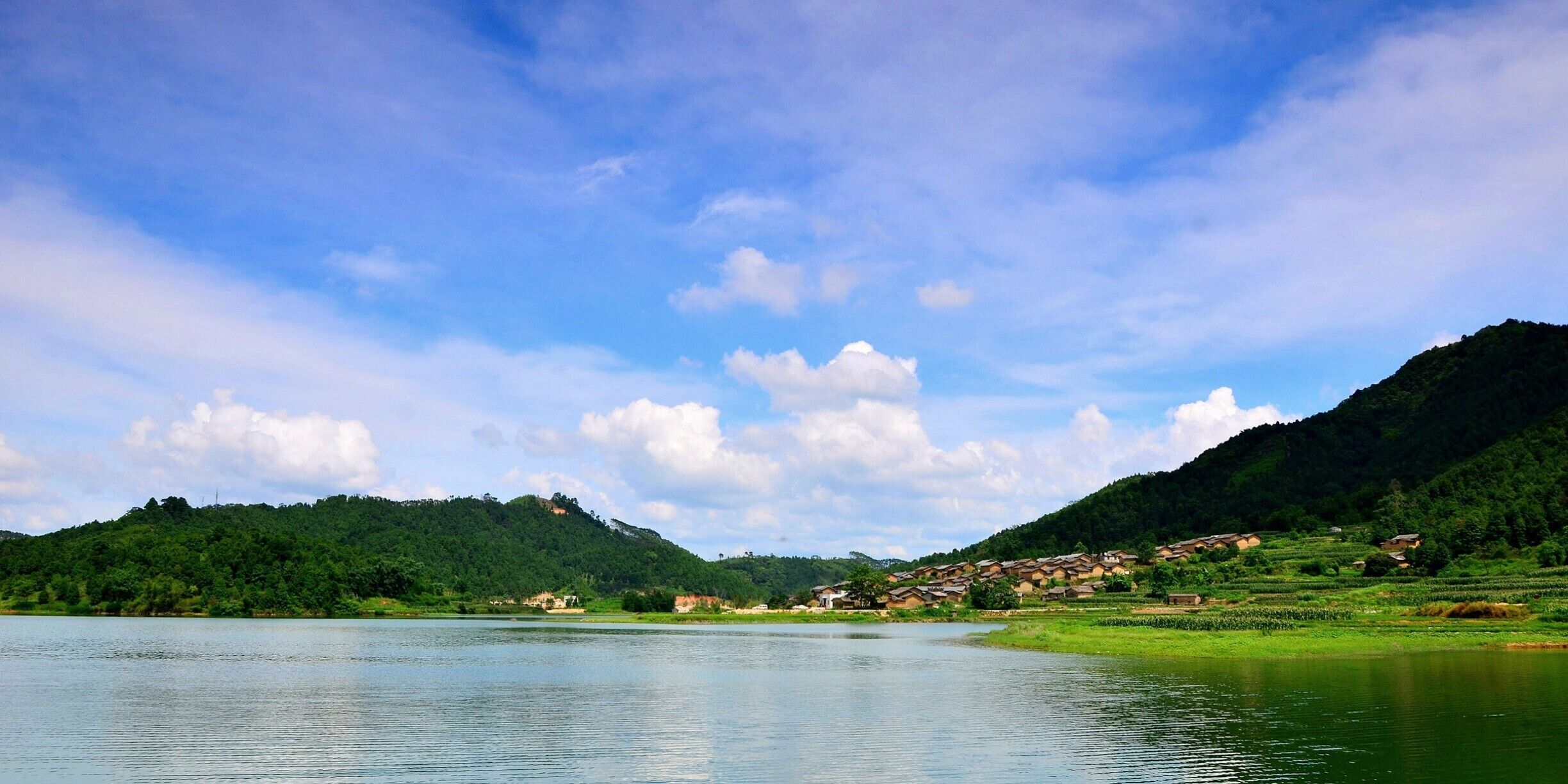 A calm lake surrounded by lush green hills and a small village.