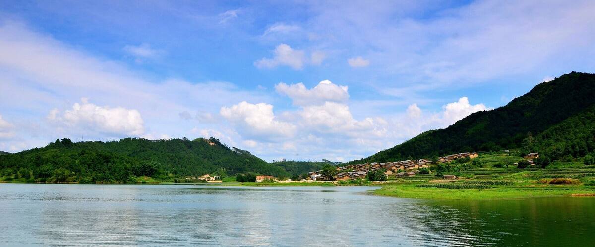 A calm lake surrounded by lush green hills and a small village.