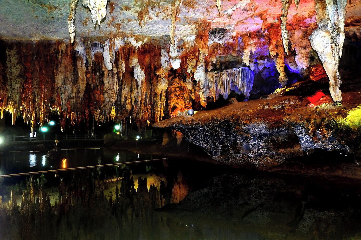 A cave with stalactites and stalagmites, illuminated by colorful lights.