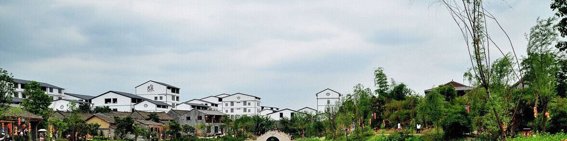 A serene pond with a stone bridge, surrounded by lush greenery and traditional buildings.