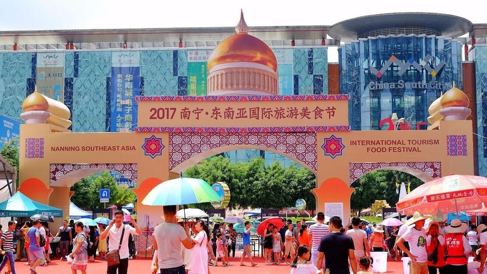 A crowded entrance to the Nanning Southeast Asia International Tourism Food Festival with a large archway and colorful umbrellas.