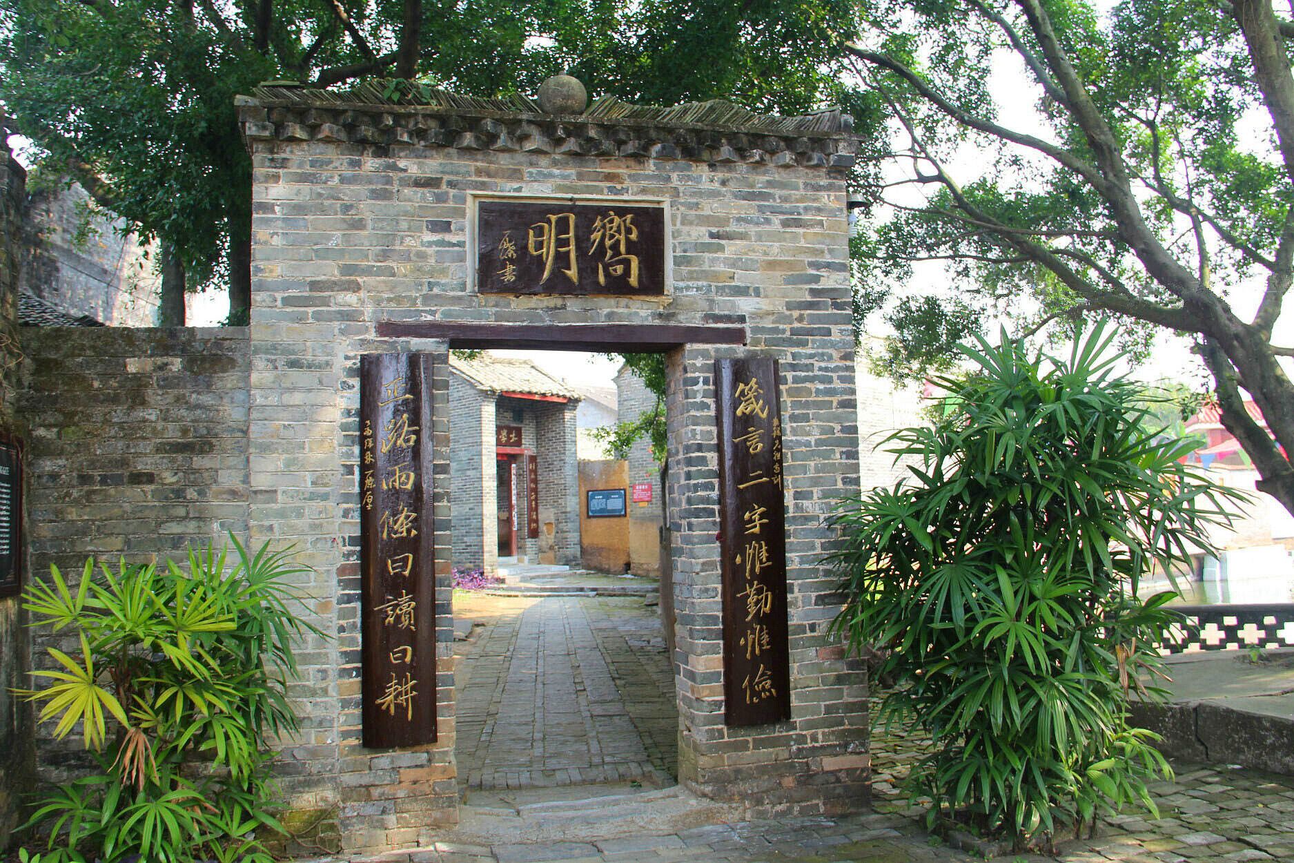 A traditional Chinese gate with inscriptions, leading to a pathway and a building in the background.